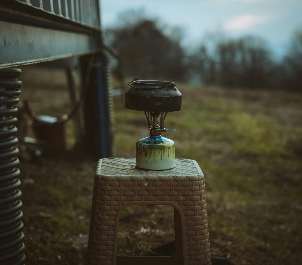 Close-up of a camping stove on a stool in a rural outdoor field setting.